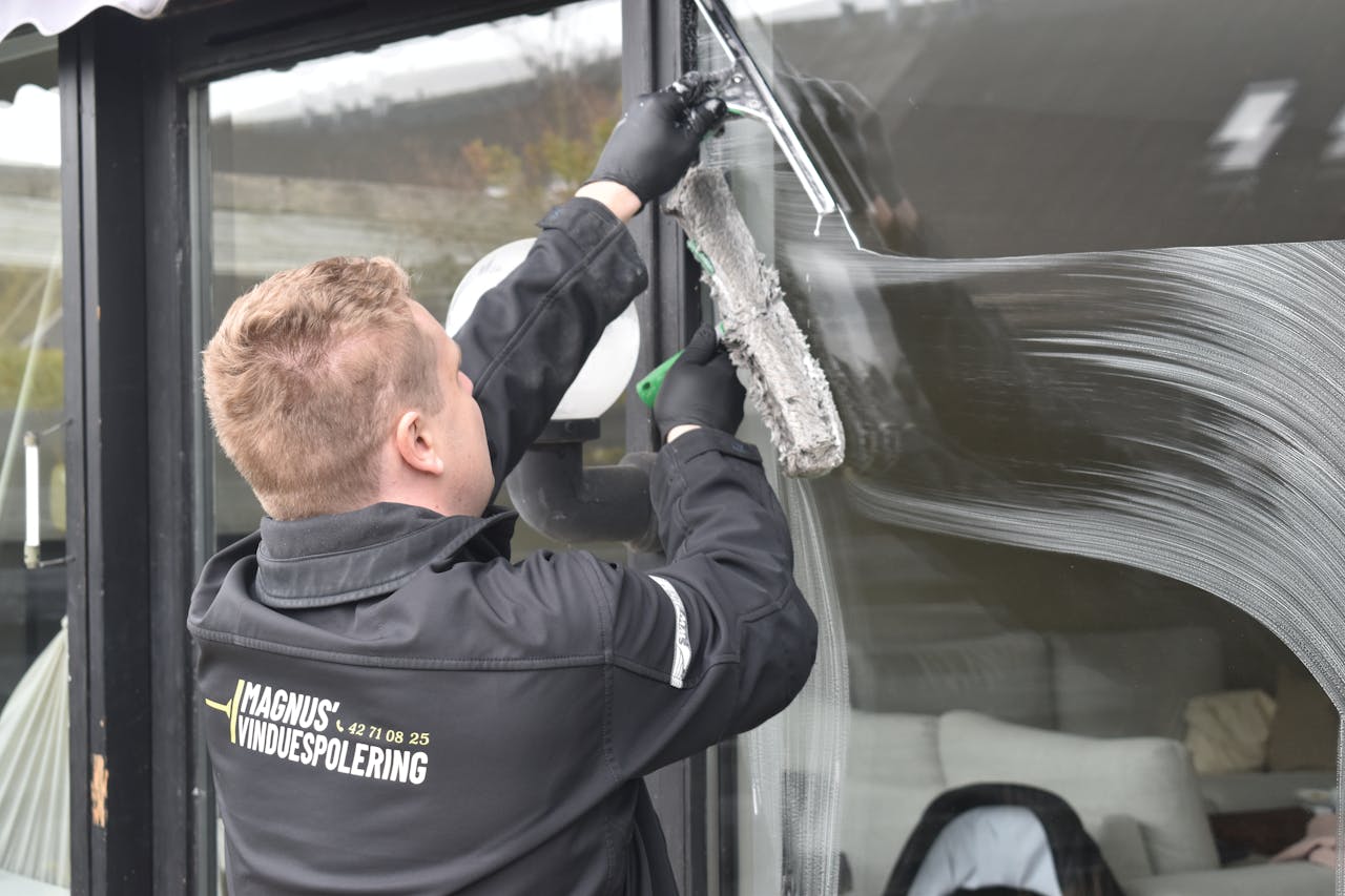 Professional cleaning service washing a large glass window. Clean and efficient work by a dedicated individual.